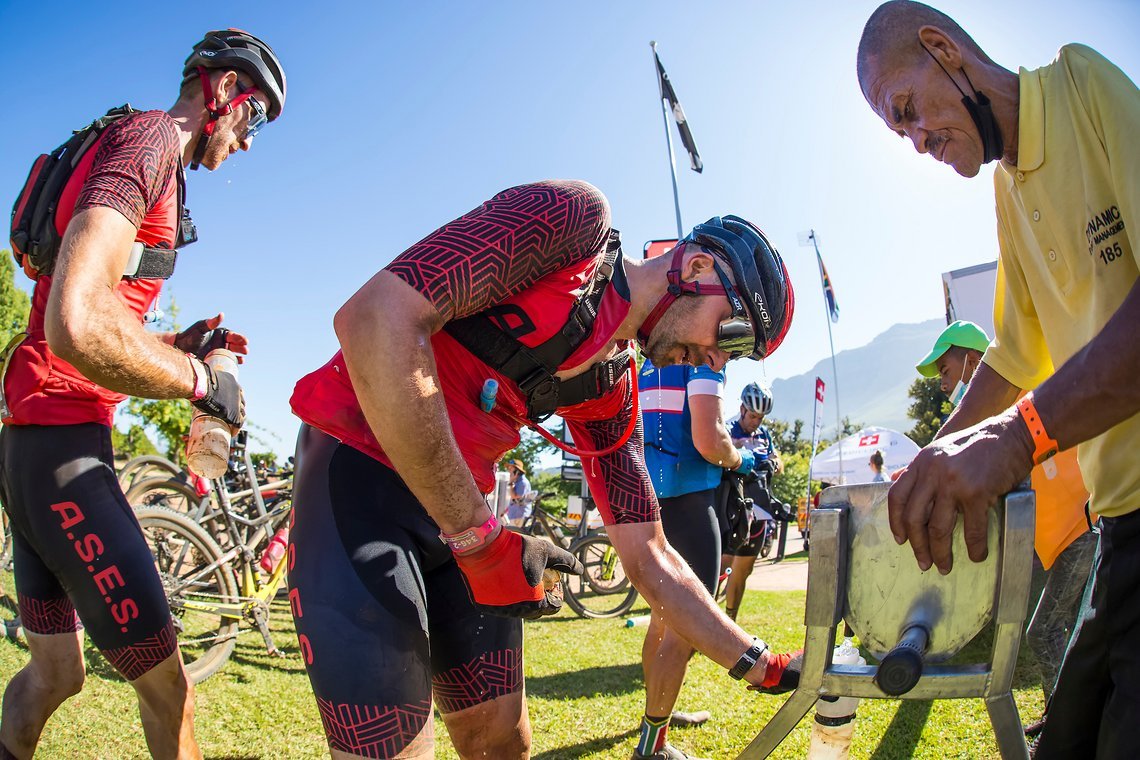 Riders filling up at Waterpoint 2 on Dornier wine estate during stage 1 of the 2022 Absa Cape Epic Mountain Bike stage race from Lourensford Wine Estate to Lourensford Wine Estate, South Africa on the 21st March 2022. © Dom Barnardt / Cape Epic