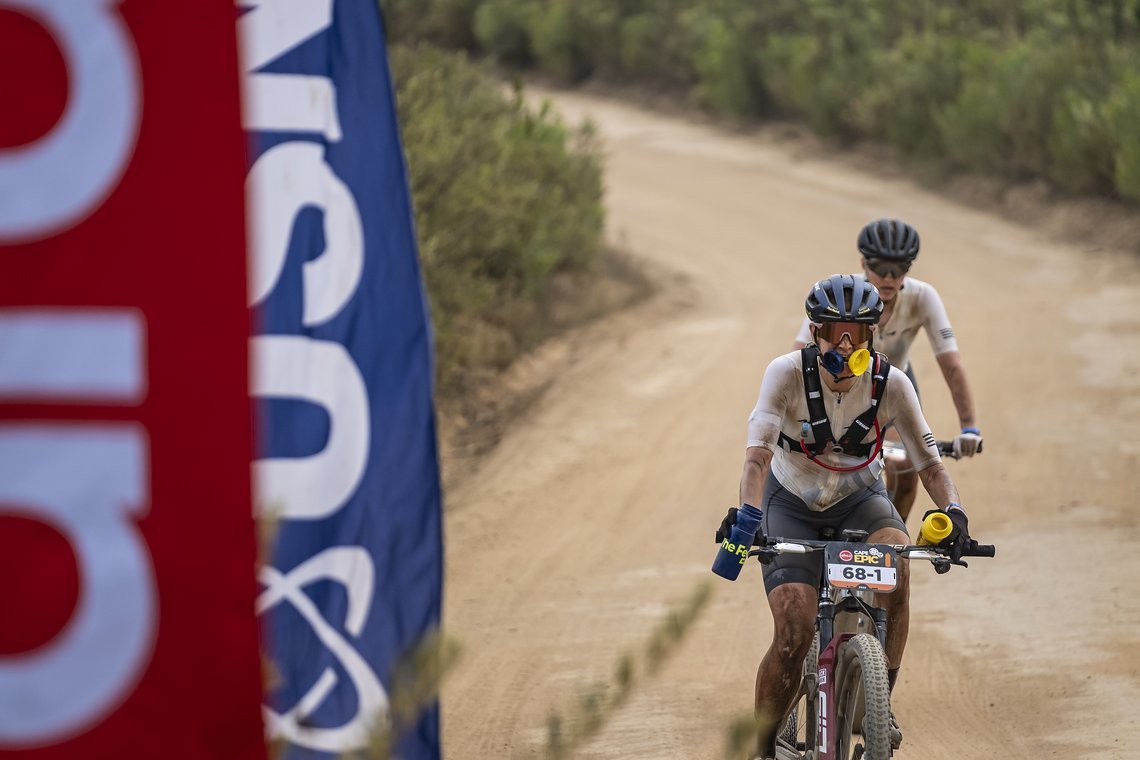 Haley Smith and Ella Boor come into the water point ready to fill up during Stage 4 of the 2025 Absa Cape Epic Mountain Bike stage race held at Fairview, Paarl, Cape Town, South Africa on the 20th March 2025. Photo by Dom Barnardt/Cape Epic
PLEASE EN